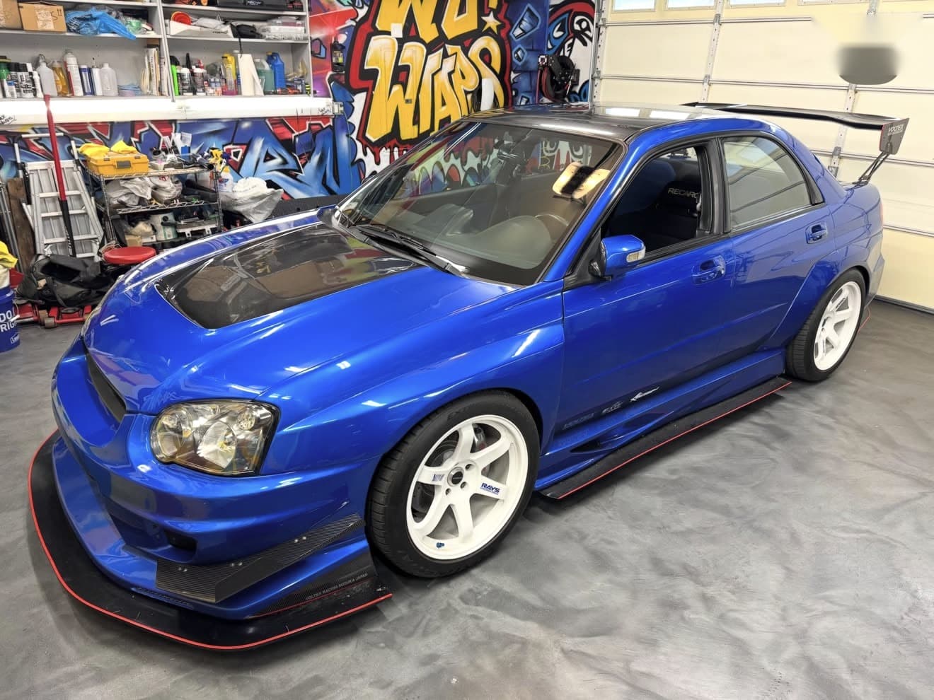 Blue Subaru WRX with a fresh gloss black roof wrap in front of the Wu Wraps mural
