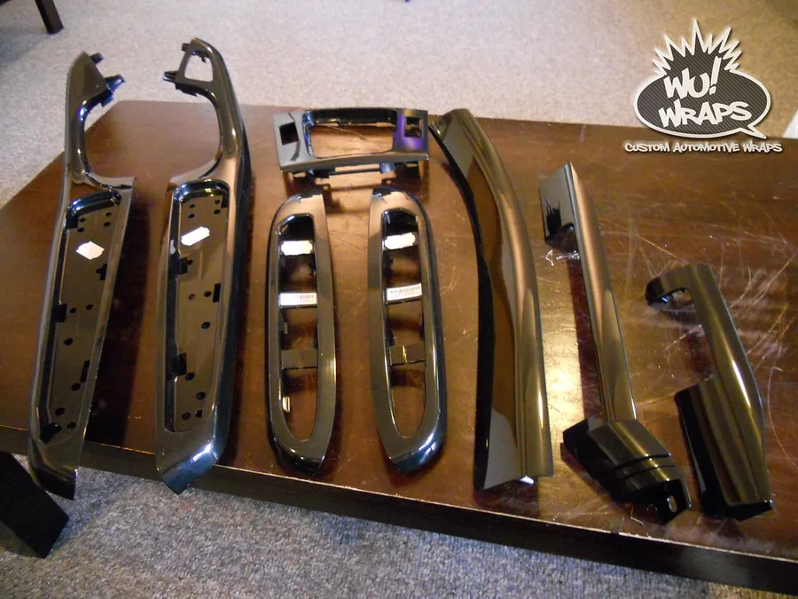 A full set of chrome BMW E46 interior trim pieces laid out in a row on a table, stripped from the car and ready to be wrapped