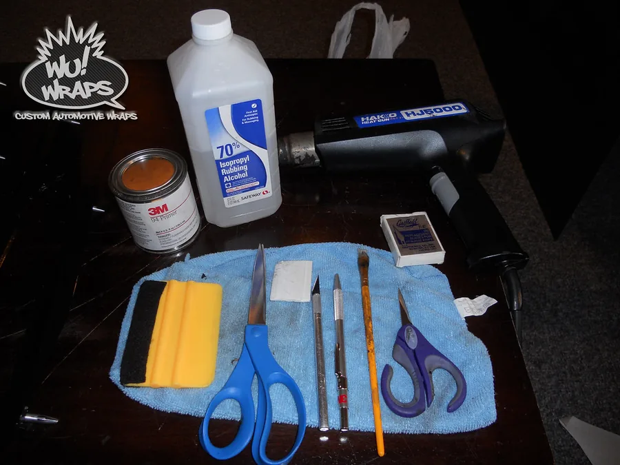 The full 2011 toolkit laid out on a blue microfiber towel: 3M primer, isopropyl alcohol, a Hakko heat gun, two squeegees, scissors, a blade and a brush